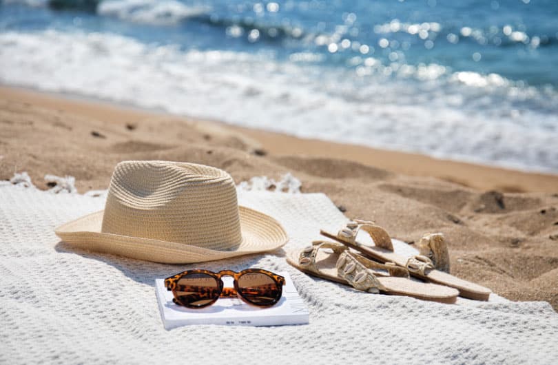 Photo of a hat, sunglasses, and sandals on the beach